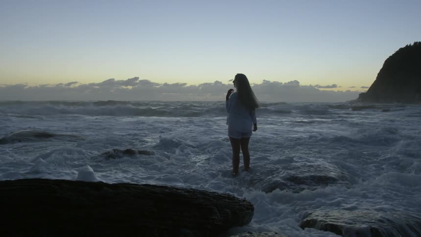 A young woman stands on the rocks as high tide begins to come in