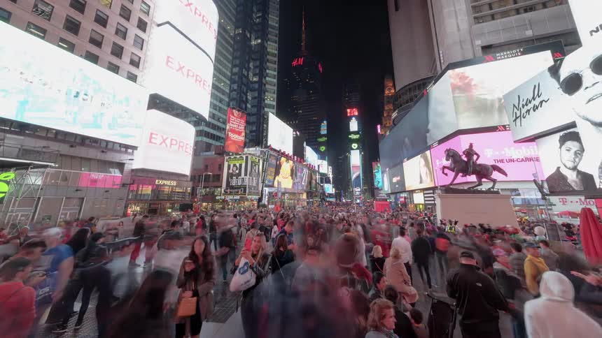 Pedestrians fill a tourist destination filled with high rise buildings and large digital screens at night