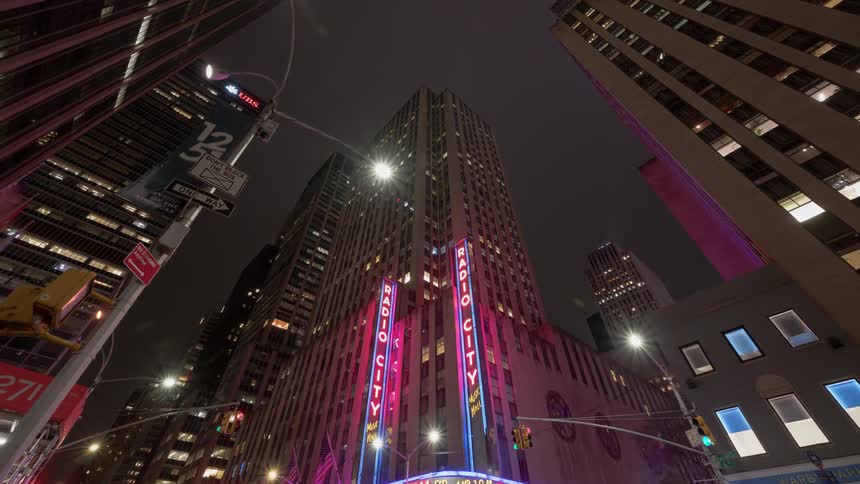 Traffic and pedestrians move through intersection under neon decorated skyscrapers