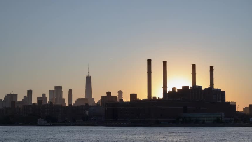 Sun sets behind factory as boats pass