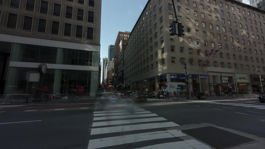 Traffic and people move through a large city intersection on a blue sky day