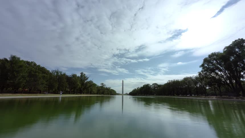 People walk the pathway beside a pond and tourist monument