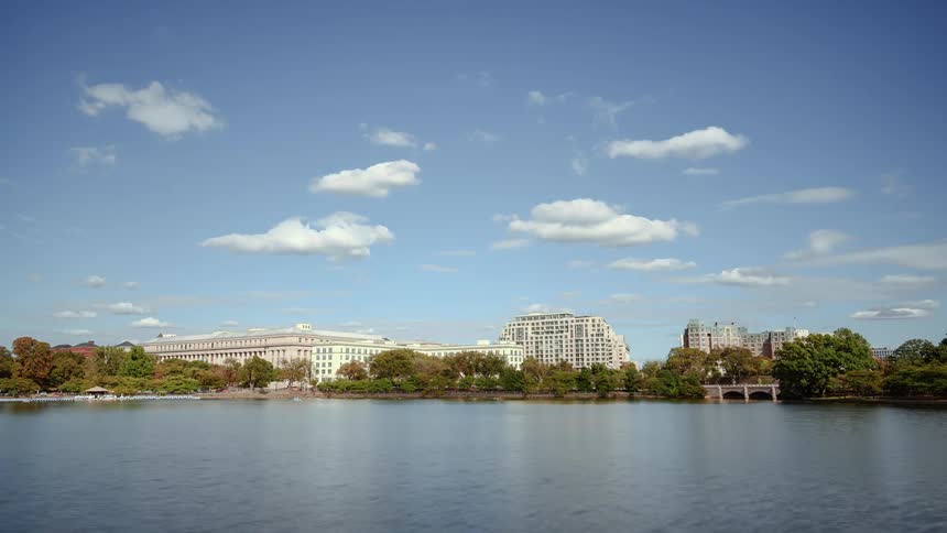 Clouds pass over lake and white buildings surrounded by trees