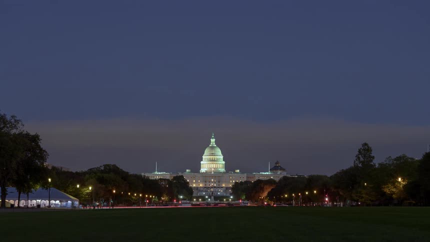 Cars travel in front of the us capitol building as the sun goes down at dusk