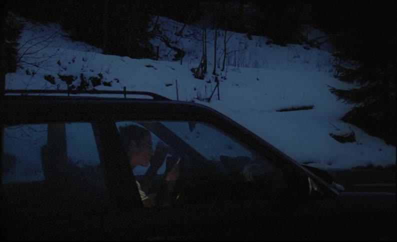 A man sits in a car along a snowy roadside yelling in his cellphone