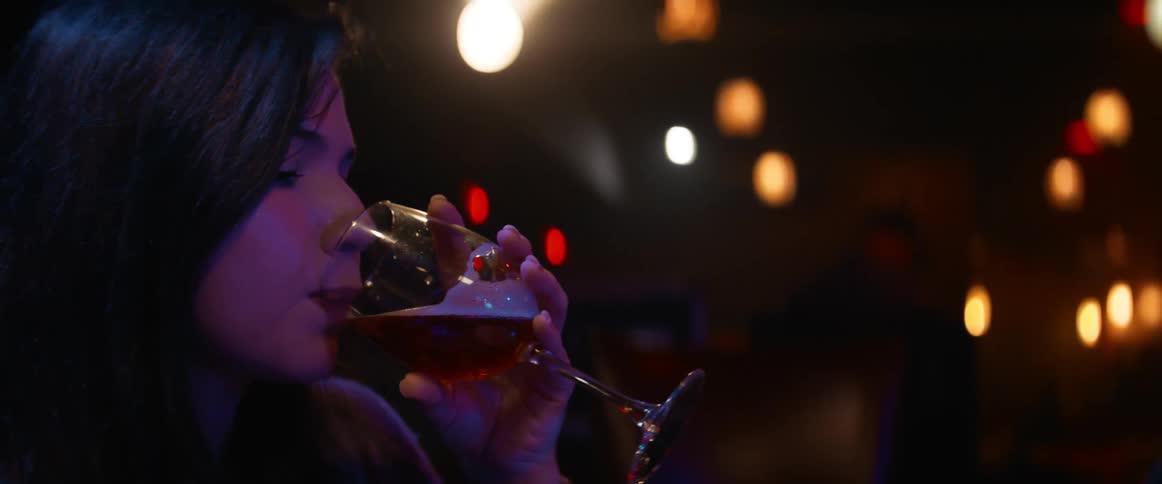 Woman drinks from wine glass in darkened room
