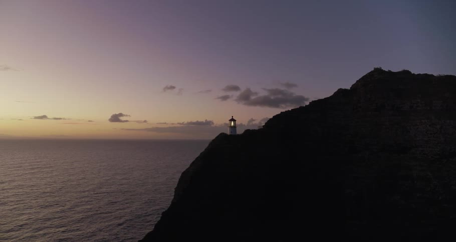 A lighthouse is lit up inside as the sun rises