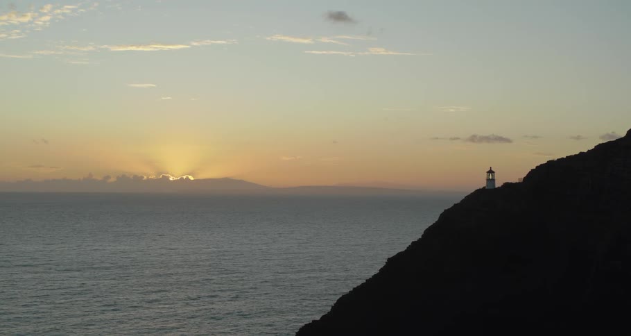 The sun shines behind a distant land beside an ocean