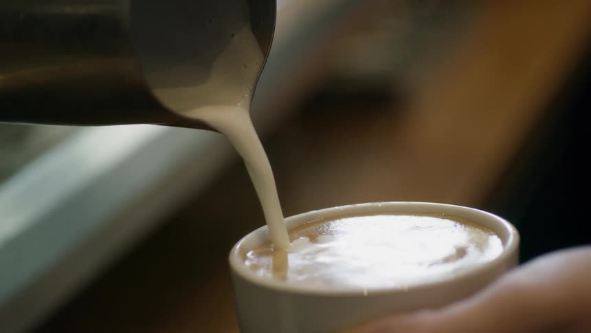 A person is pouring creamer in a coffee cup
