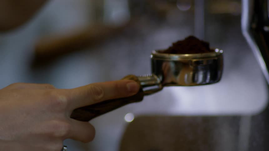 A person holds espresso grounds in a container