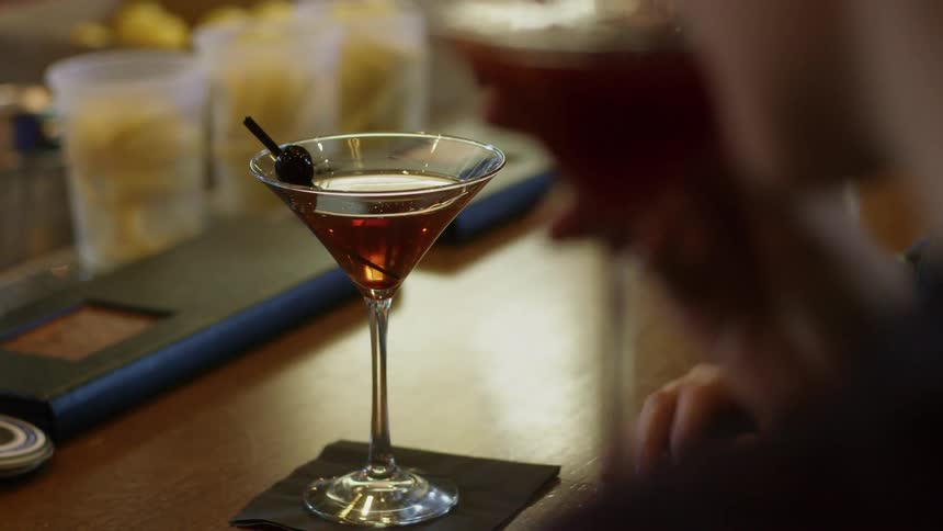Two people in suits drink martinis at a bar