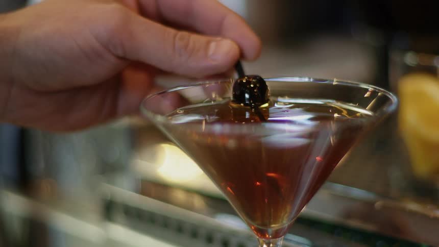 A person puts an olive in to a martini