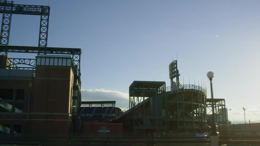 The exterior of a baseball field in the city with seats and lights visible