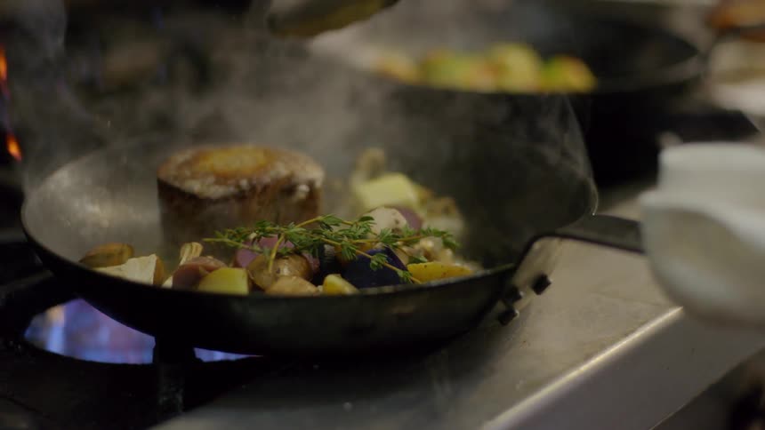 A cook flips a steak in a restaurant kitchen