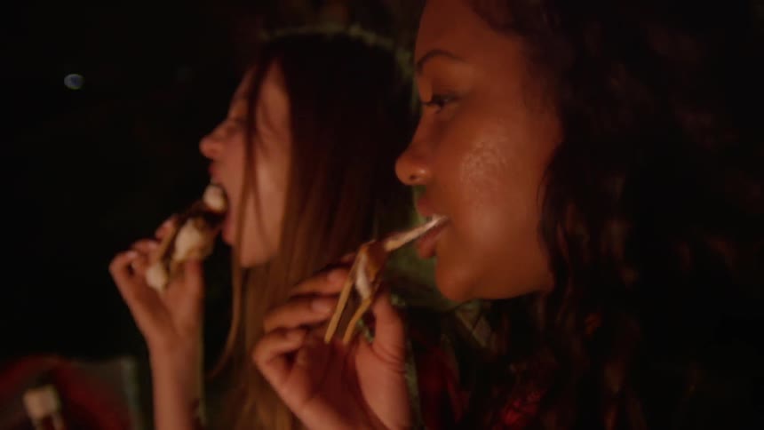 Two women eat smores outside at night