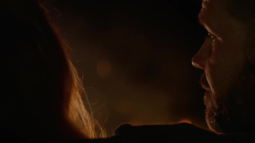 A man and woman sit in front of a fire at night and talk