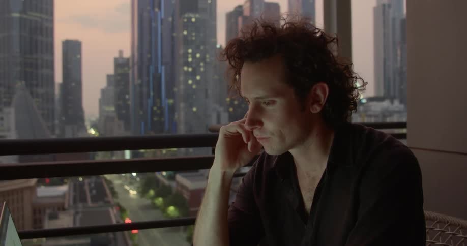 Man sits working on laptop next to window showing downtown skyscrapers
