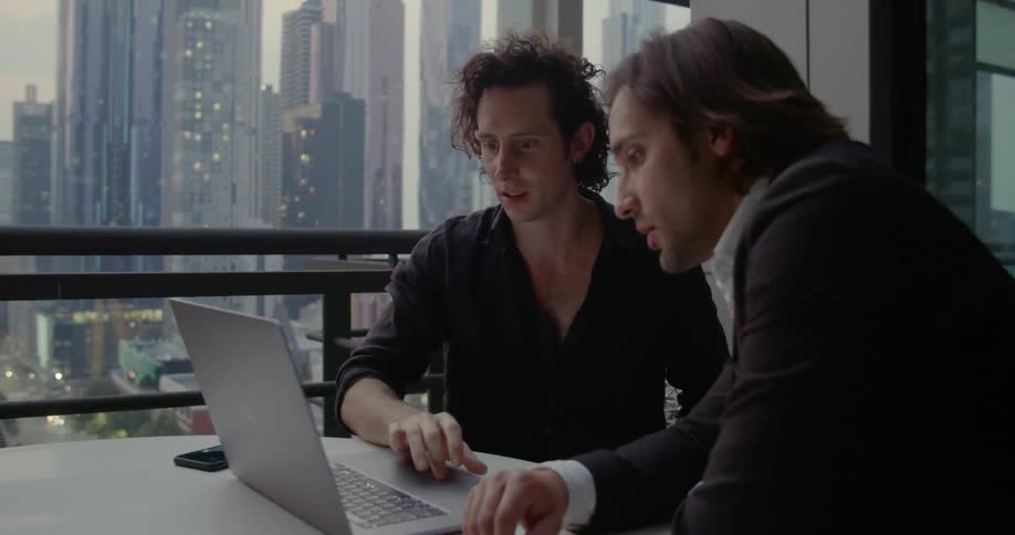 Two men work on a laptop in a high rise building