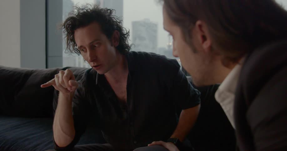Two men sit on a couch and talk together