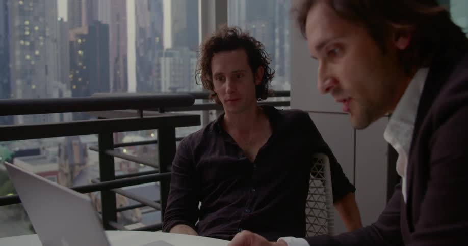 Two men sit at a desk and work on a laptop