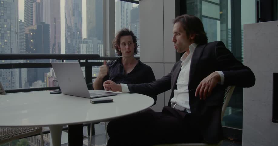 Two men sit at a table and work on a laptop