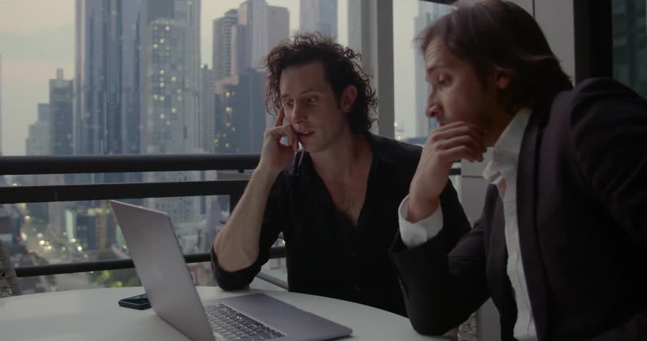 Two men sitting at a table looking at a laptop