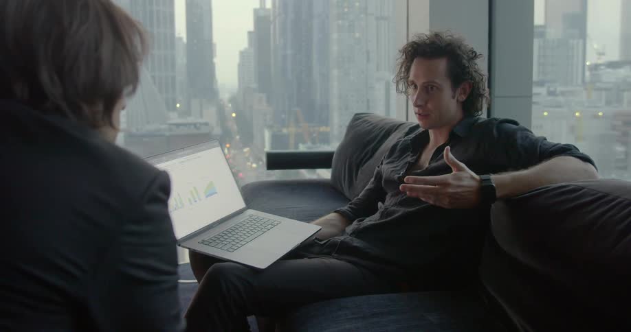 Two men discuss graphs near large windows with city view