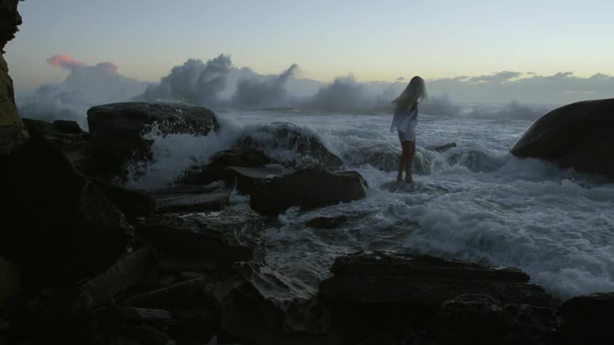 A woman being hit by waves on a rocky shore