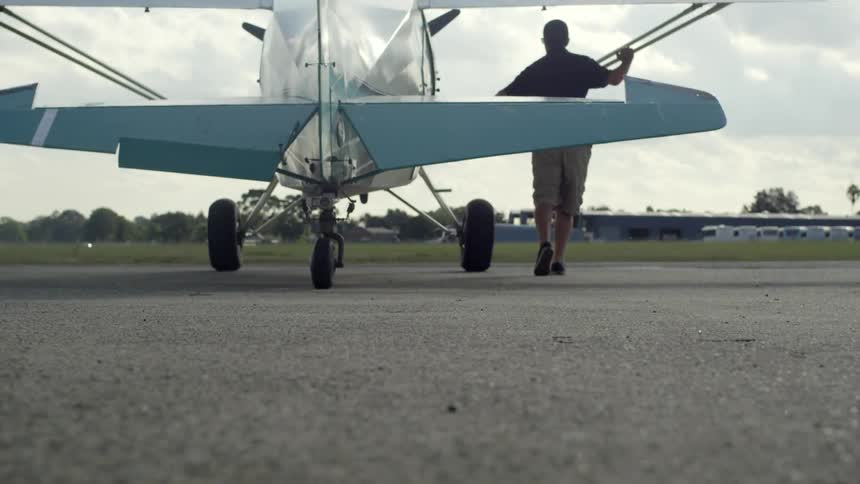 A man pushing a small plane along asphalt