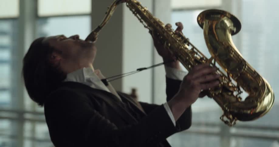 A man plays a saxophone in a an open office type room