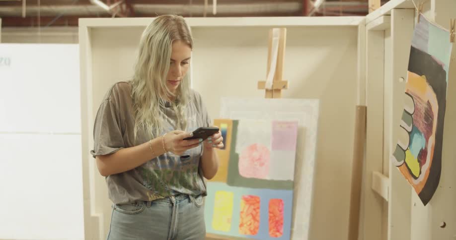 A young woman takes pictures of a painting with her cellphone