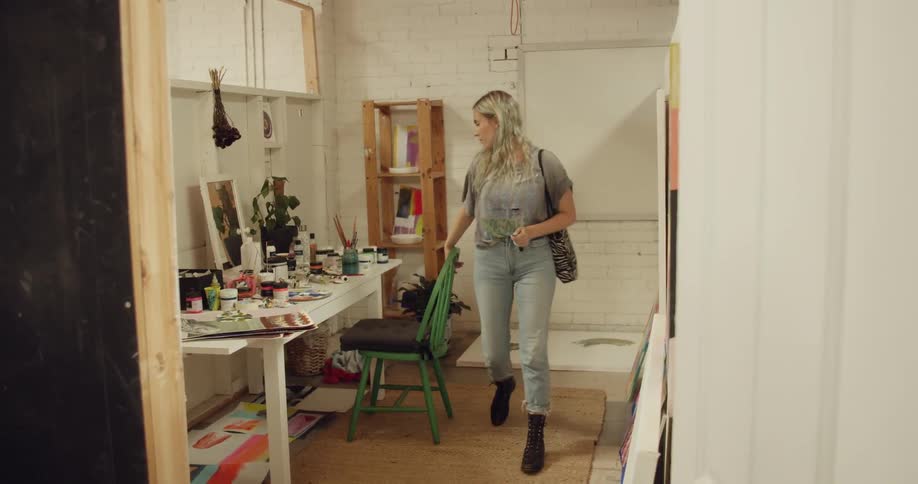 A young white woman turns off a light in a room and then leaves through the door
