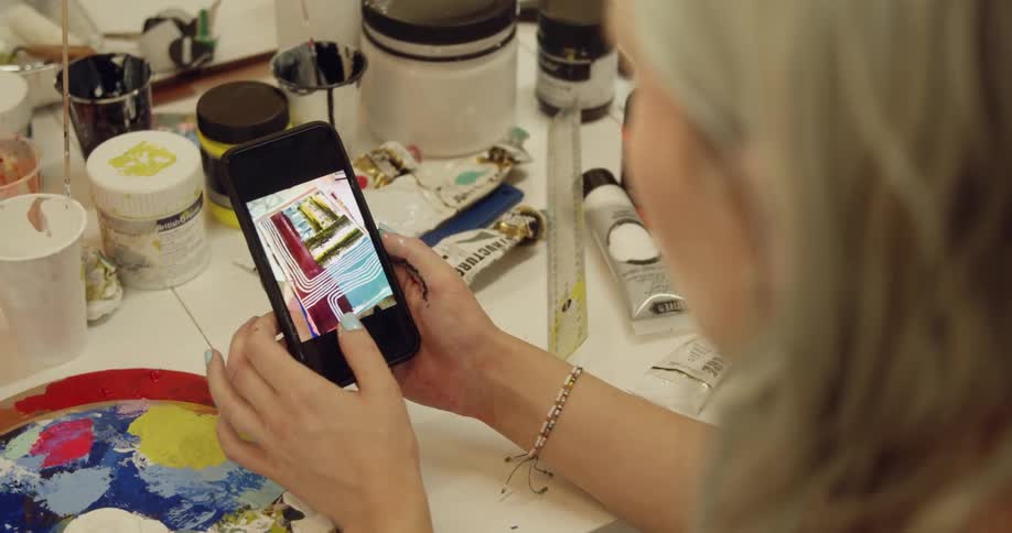 A white woman sits at a table and swipes through a smartphone