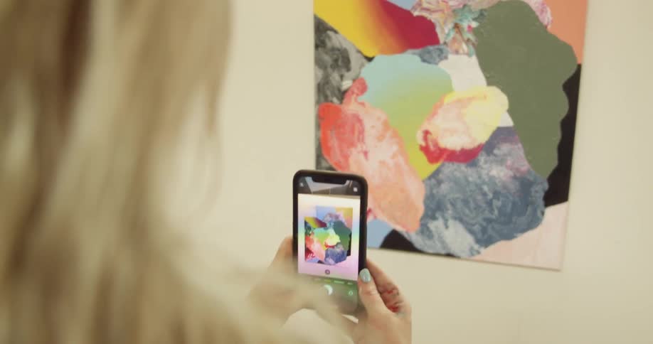 A woman uses her cellphone to take a picture of a painting
