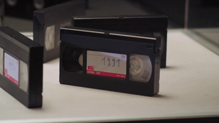 Vhs tapes labeled with years stand on end on a mirror backed shelf