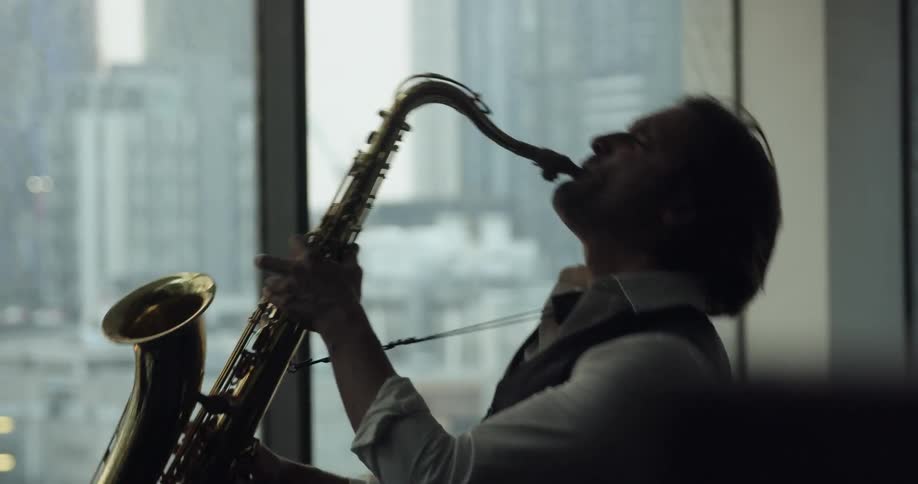A man standing next to a window playing a saxophone