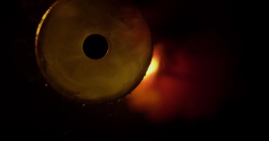 Bronze metal disk with center hole moved from in front of glow surrounded by darkness