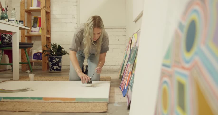 A woman pours paint onto a canvas on the floor