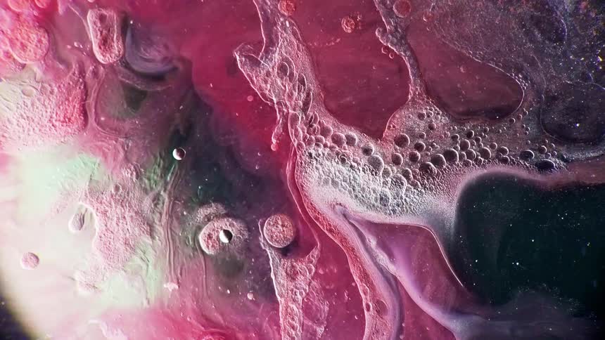 A drop falls into a cloudy and foamy colorful liquid causing ripples
