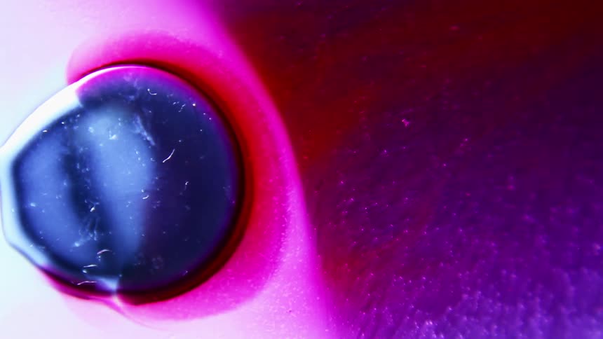 A reddish pink fluid flows outward and begins to surround a smaller blue droplet
