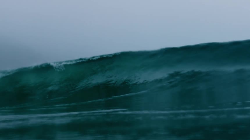 A large blue green wave breaking on a rainy day