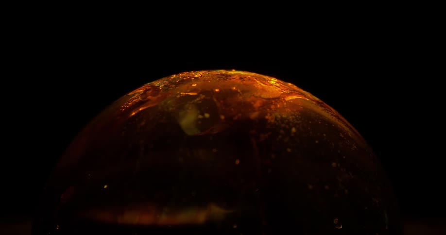A liquid sphere with an orange hue appears to a have rippling and mixing across its surface