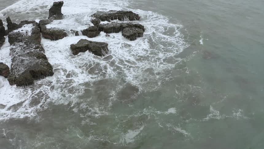 Waves crashing into black rocks in the ocean near the shoreline