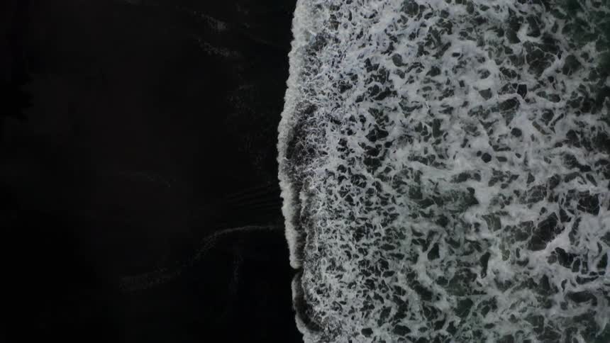 Aerial view of waves crashing on the black sand beach