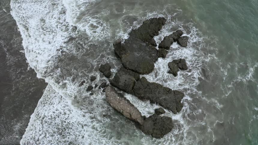 Aerial view of ocean waves crashing in the rocks of a beach