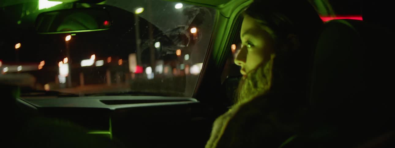 A young woman riding in the passenger seat of a vehicle at night