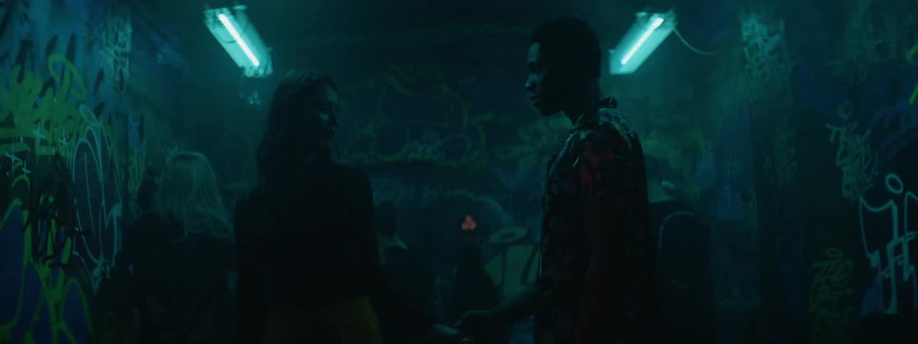 A black man and a white woman walk out onto a dance floor in a dingy nightclub