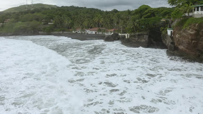 Foamy waves crash along a rocky shore near an estate
