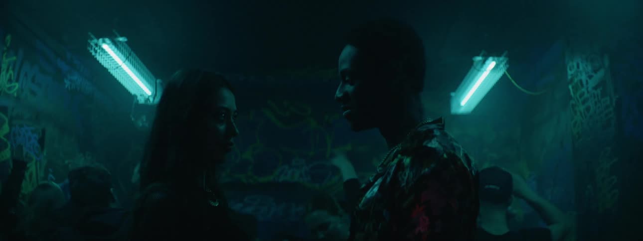 A young man and woman talk in a club as people dance behind them