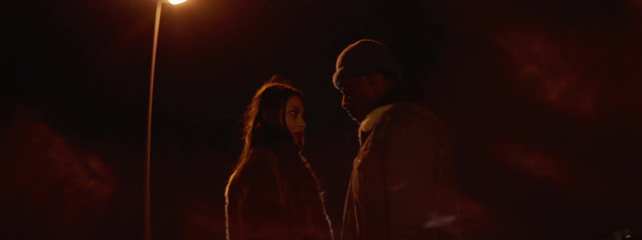 Couple standing under a street lamp at night staring at each there